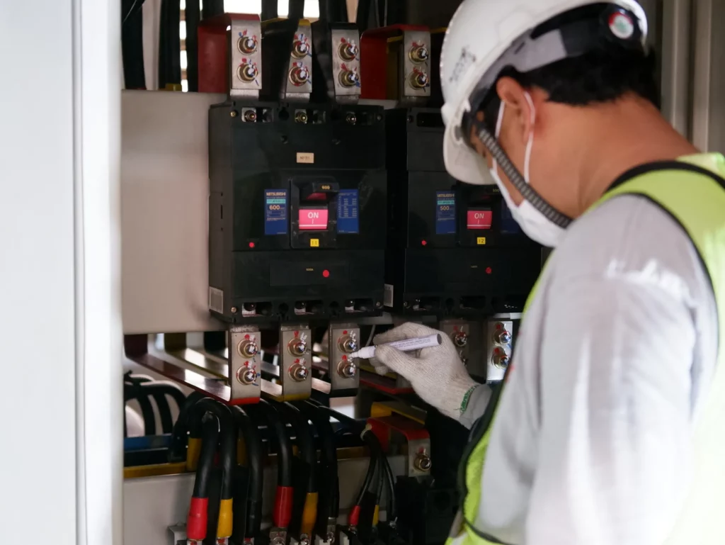 Störungsmanagement: Elektrofachkraft mit Schutzhelm und Handschuhen prüft Leistungsschalter in einem Schaltschrank