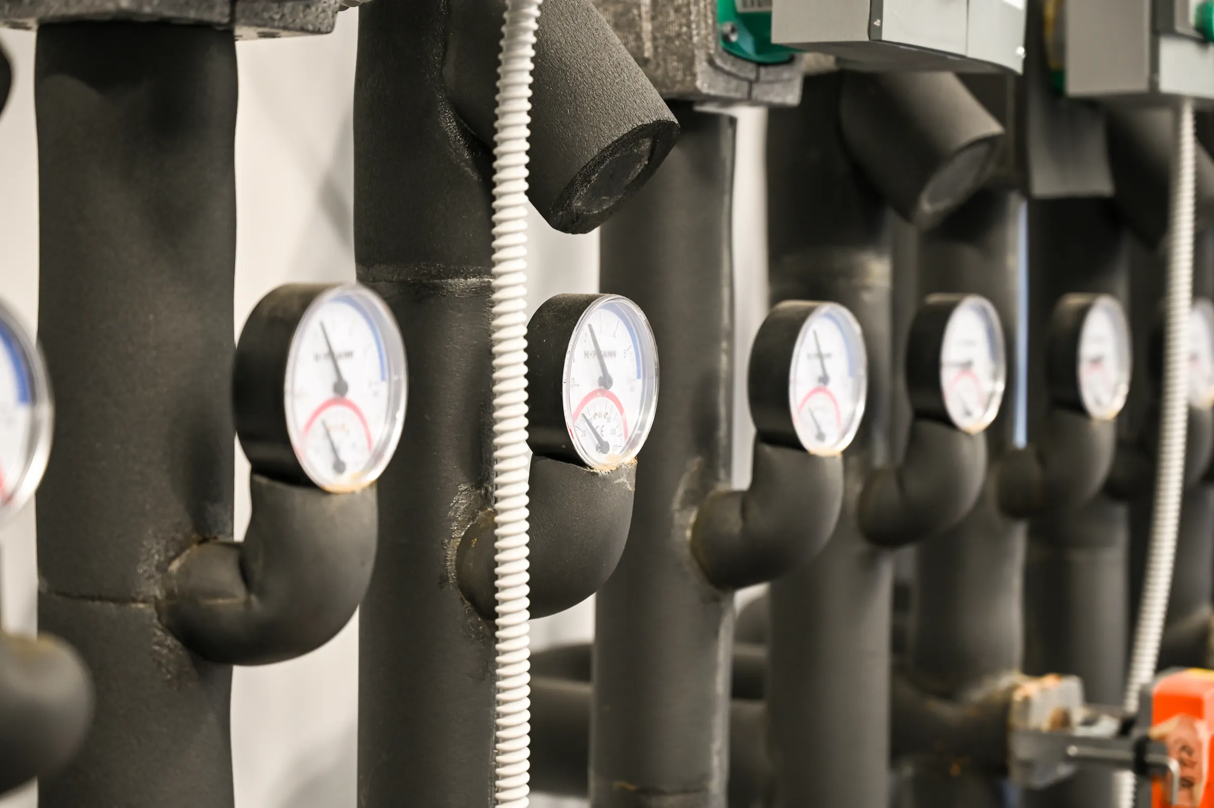 Gesetzliche Prüfungen: gedämmte Heizungsrohre mit einer Reihe von Thermomanometern im Technikraum