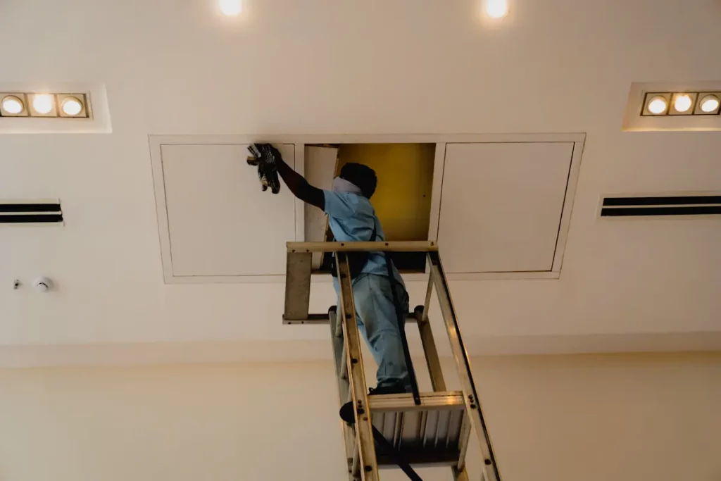 Haustechniker auf einer Leiter arbeitet an einer Revisionsklappe in der Decke