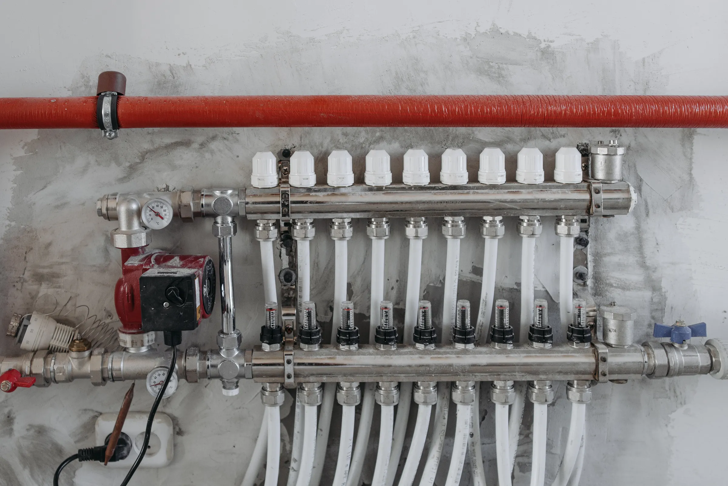 Verbrauchsoptimierung: Heizkreisverteiler mit Pumpe, Durchflussanzeigern und Manometer an einer Wand