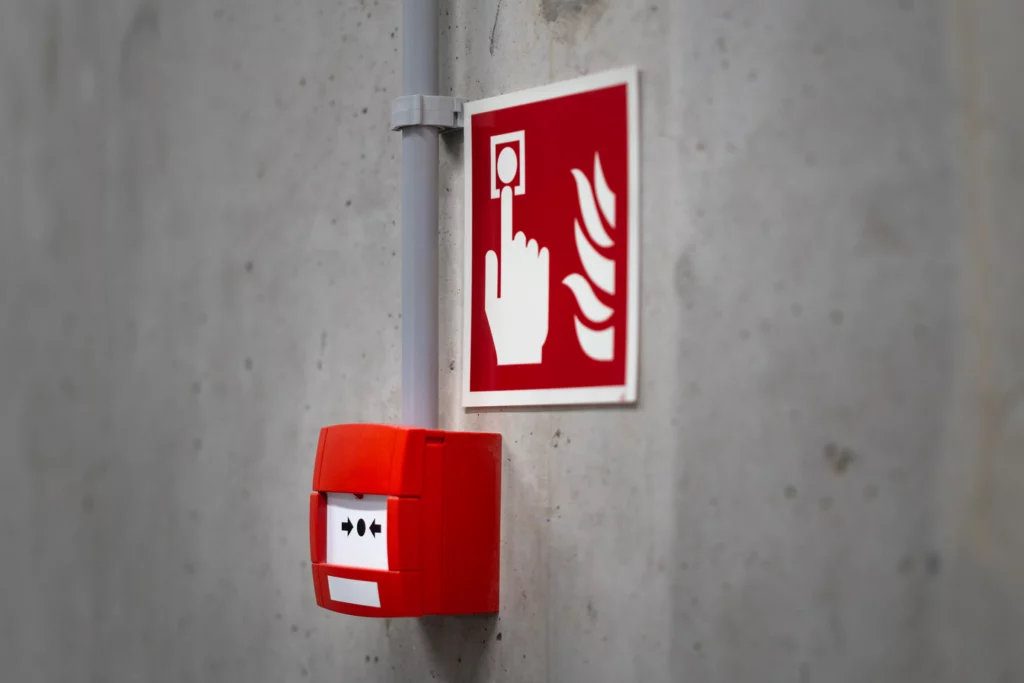 Roter Handfeuermelder mit Hinweisschild an einer Betonwand