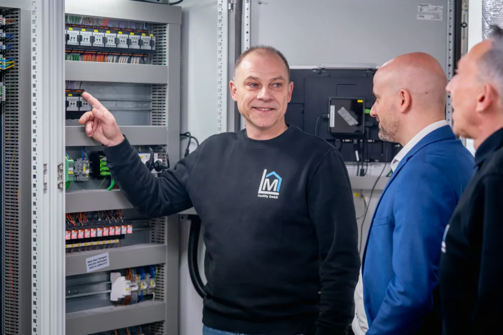 Technisches Facility Management: Techniker von ML Facility erklärt Kollegen die Komponenten eines Schaltschranks