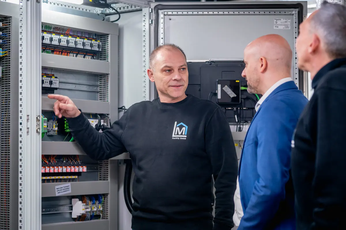 Techniker von ML Facility zeigt auf Bauteile im geöffneten Schaltschrank